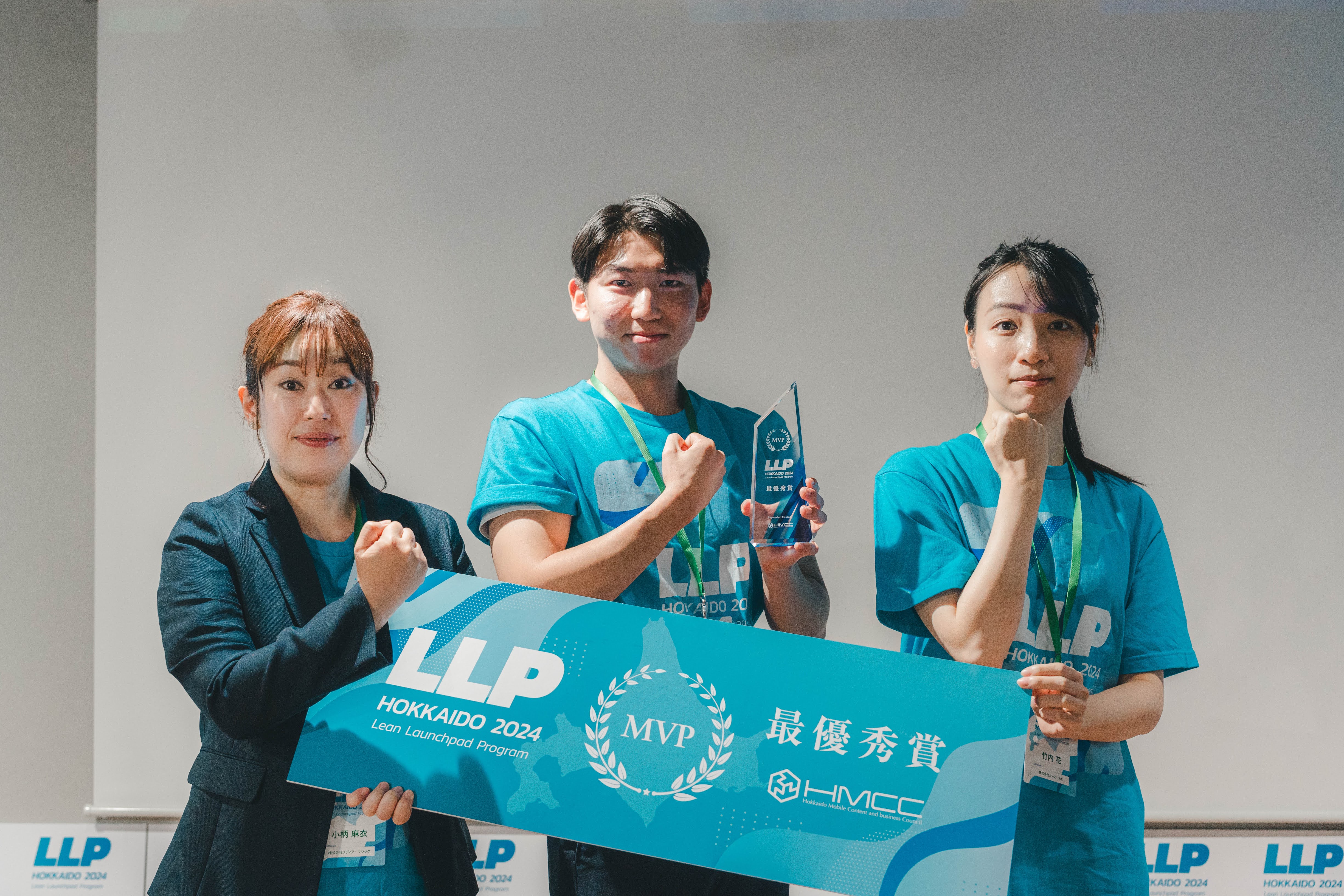 2024年の優勝チームの集合写真 左から女性、男性、女性と並ぶ 両端の女性が左手で「LLP最優秀賞」と記載された看板を持ち、真ん中の男性が左手でトロフィーを持ち、全員で右手でガッツポーズをしている